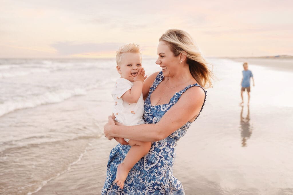 Mother embraces her baby on Isle of Palms Beach during Family Portrait Session with, Holy City Family Photography in Charleston, SC.