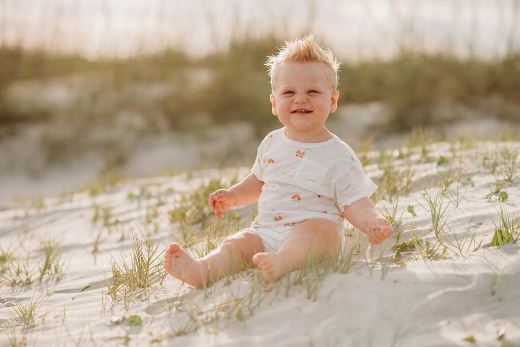 Baby smiles at the camera on Isle of Palms Beach during Family Portrait Session with, Holy City Family Photography in Charleston, SC.