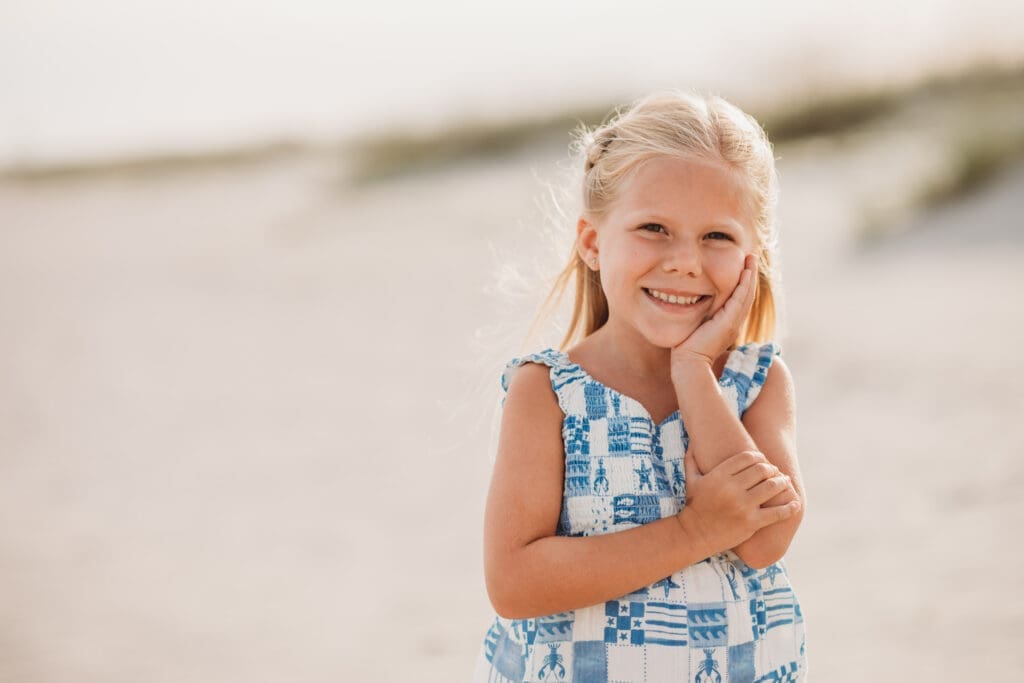 Little girl smiles at the camera during summer, sunset beach mini sessions on Folly Beach with Holy City Family Photography after searching for Charleston Mini Sessions.