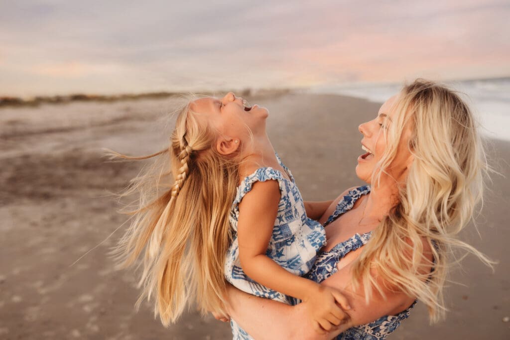 Mother embraces her daughter for summer, sunset beach mini sessions on Folly Beach with Holy City Family Photography after searching for Charleston Mini Sessions.