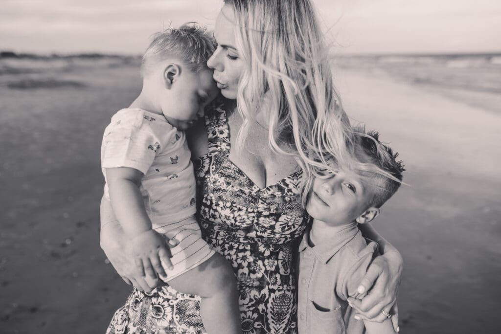 Mother embraces her sons for summer, sunset beach mini sessions on Folly Beach with Holy City Family Photography after searching for Charleston Mini Sessions.