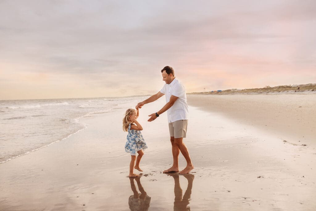 Father dances with his daughter on Isle of Palms Beach during Family Portrait Session with, Holy City Family Photography in Charleston, SC.